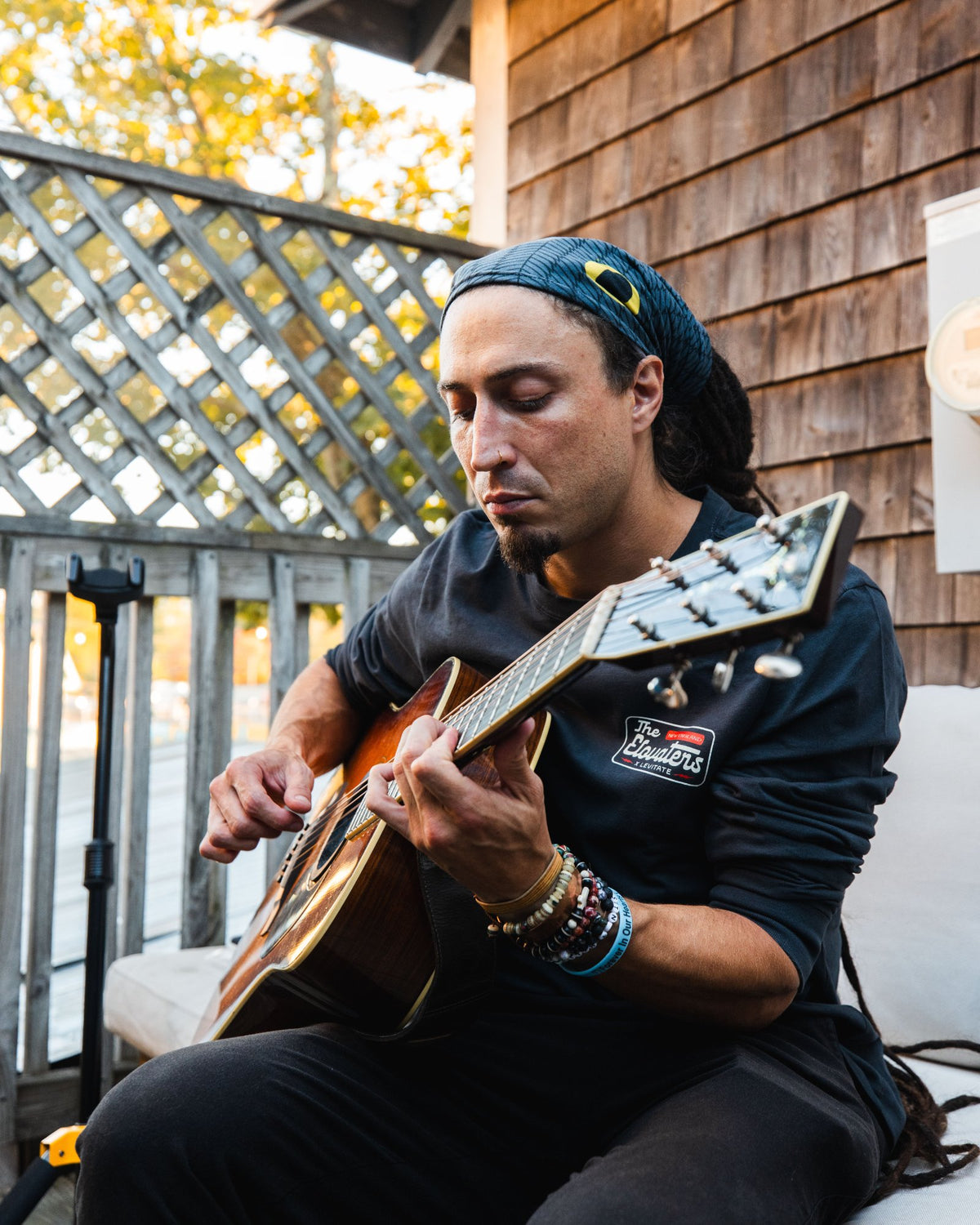Member of The Elovaters playing acoustic guitar on the Backyard patio in the new collab tee