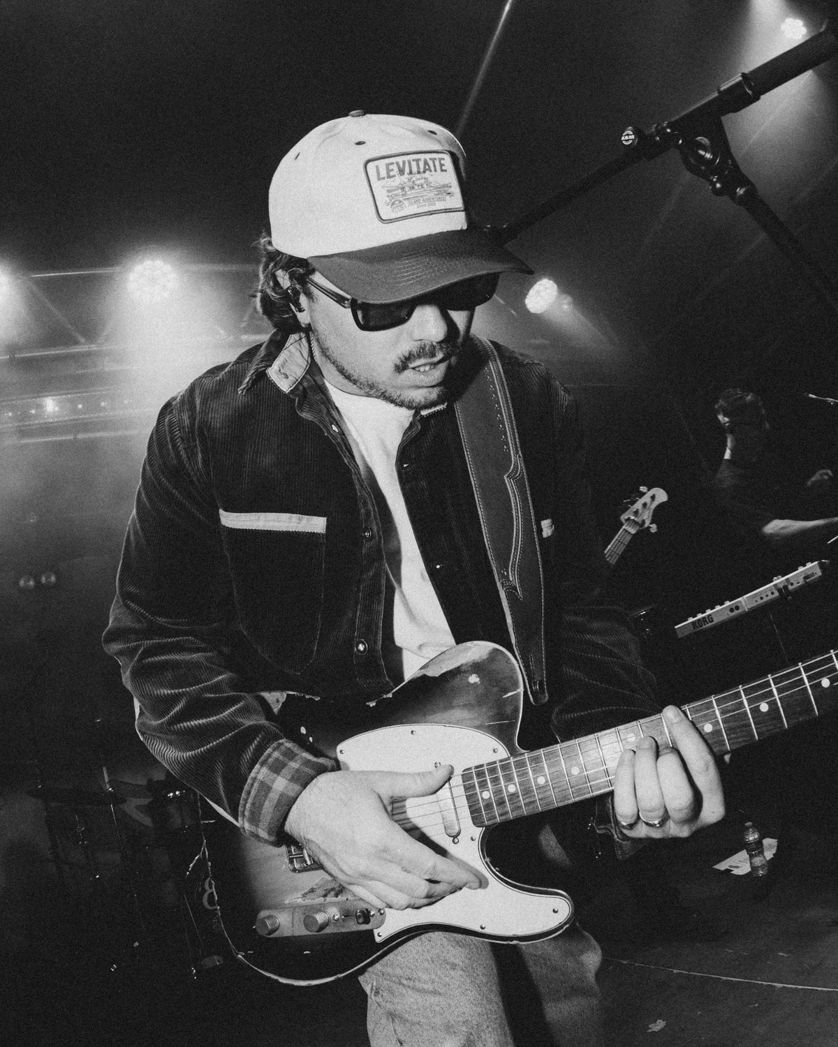 Black-and-white shot of The Elovaters' guitarist in a Levitate trucker hat playing a Telecaster