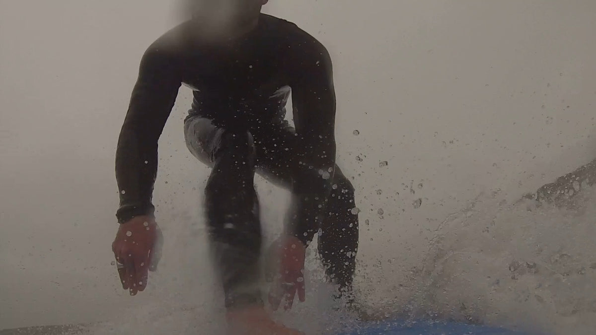 GoPro view from the nose of a surfboard as a surfer pops up in the whitewater