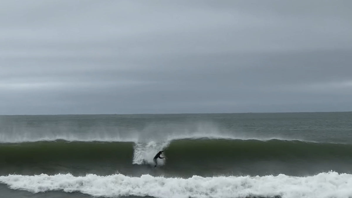 Surfer dropping into a wave behind Cisco on Nantucket on a gray October morning