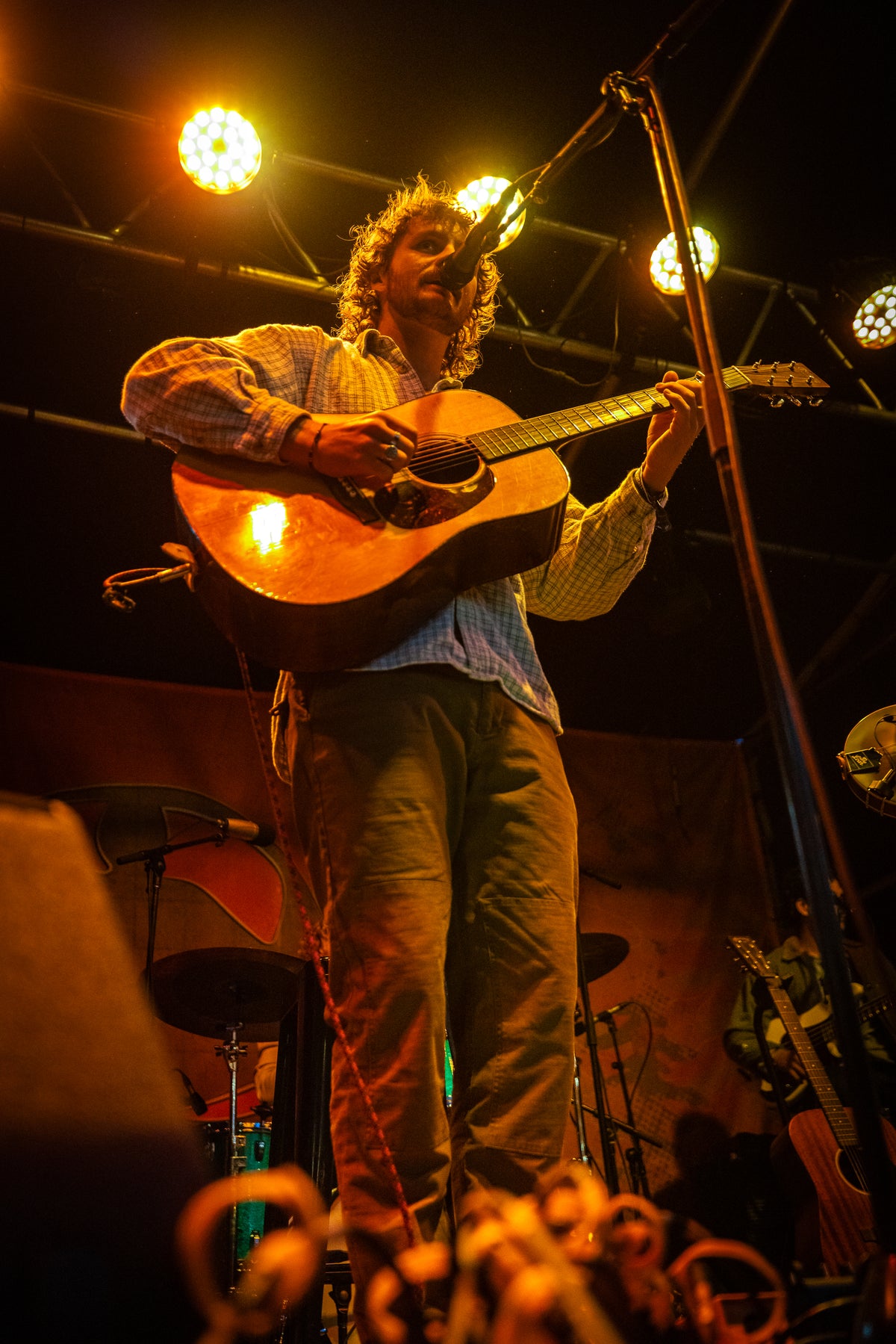 Evan Honer playing acoustic guitar under the stage lights at Flannel Jam in Marshfield